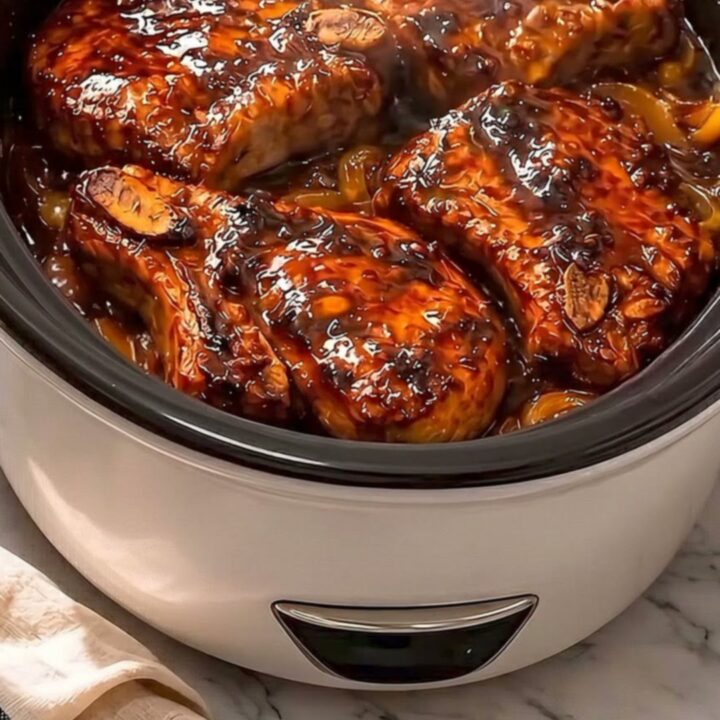 Four caramelized honey garlic pork chops resting in a slow cooker with steam rising.
