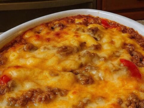 A steaming scoop of cheesy beef macaroni casserole showing a long cheese pull and bubbly golden-brown crust.