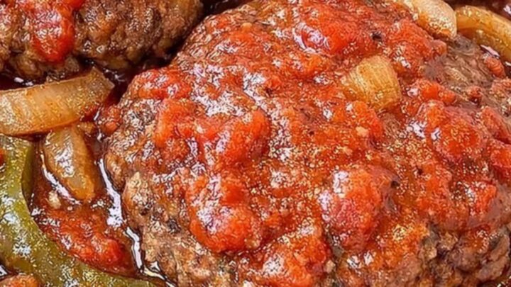 A close-up of a tender Salisbury steak patty covered in rich, thick tomato and onion gravy.