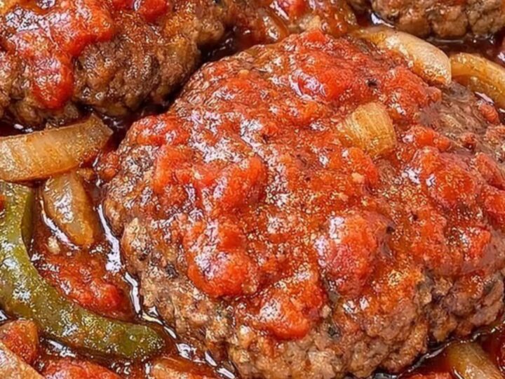 A close-up of a tender Salisbury steak patty covered in rich, thick tomato and onion gravy.