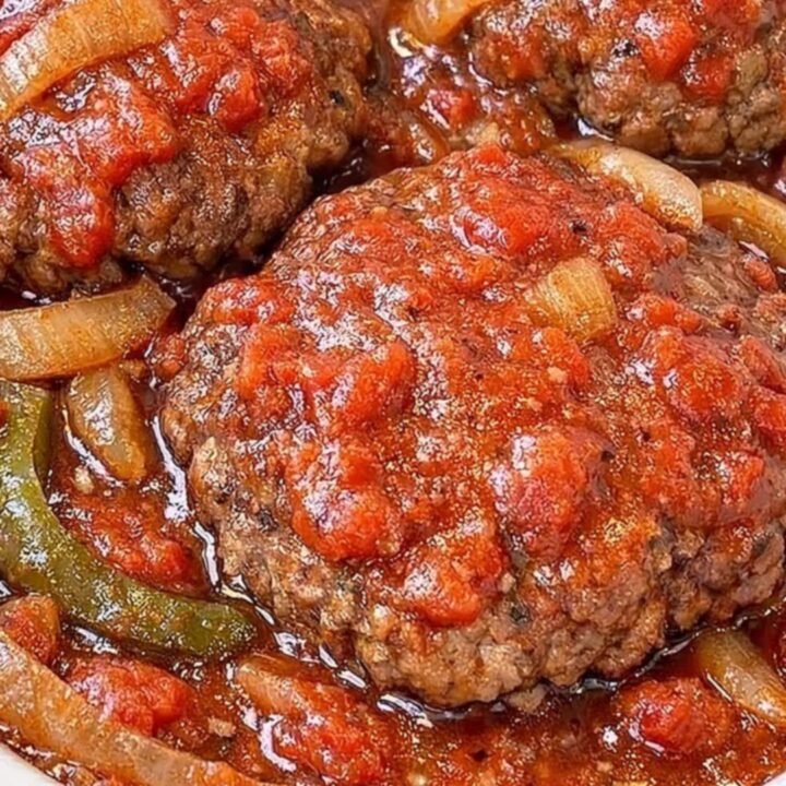 A close-up of a tender Salisbury steak patty covered in rich, thick tomato and onion gravy.