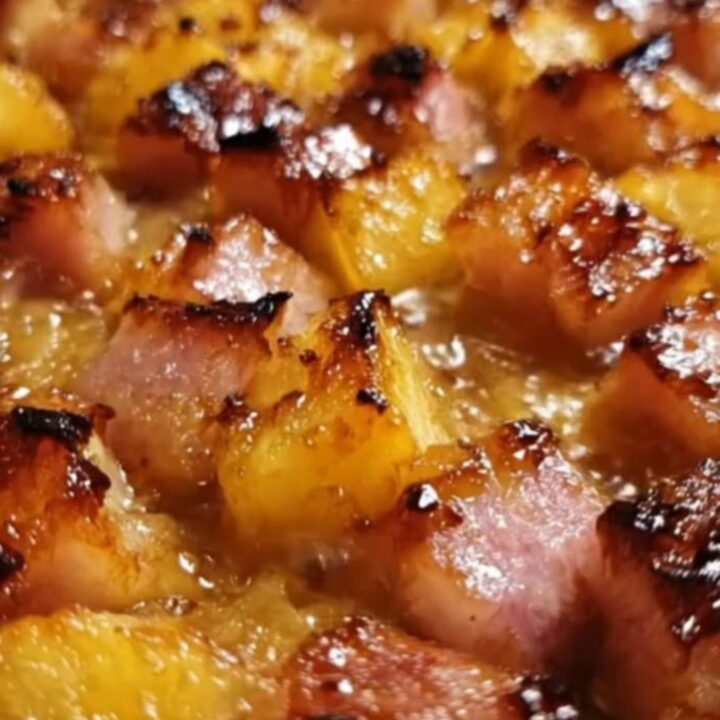A white baking dish filled with caramelized, glossy ham cubes and pineapple chunks, steam rising from the dish.