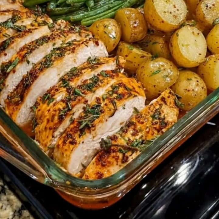 A clear glass baking dish filled with roasted chicken breast, green beans, and golden baby potatoes.