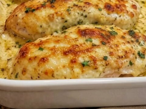 Four golden-brown, cheesy garlic parmesan chicken breasts in a white rectangular baking dish.