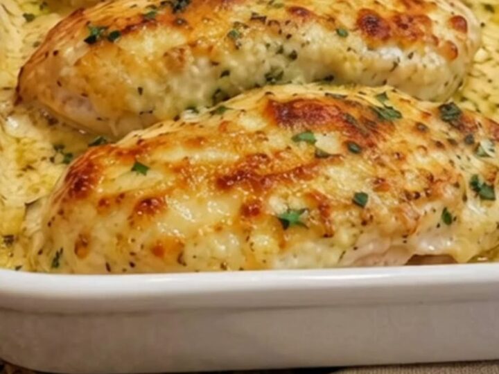 Four golden-brown, cheesy garlic parmesan chicken breasts in a white rectangular baking dish.
