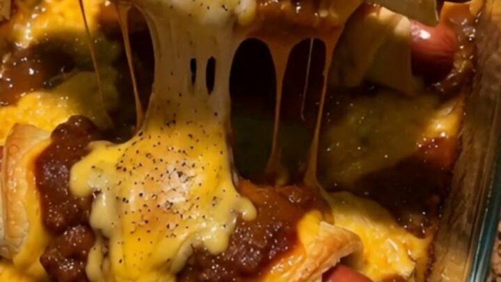 A close-up of a cheesy chili dog crescent roll showing a long, gooey cheese stretch.