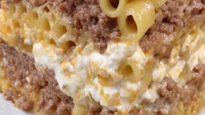 A tall, beautiful slice of golden-brown pastitsio on a decorative plate showing distinct layers.