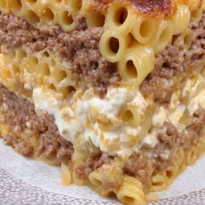 A tall, beautiful slice of golden-brown pastitsio on a decorative plate showing distinct layers.