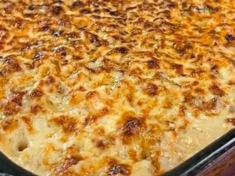 A hot spoonful of chicken and mashed potato casserole being lifted from a baking dish, showing melted cheese stretch.