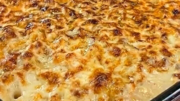 A hot spoonful of chicken and mashed potato casserole being lifted from a baking dish, showing melted cheese stretch.