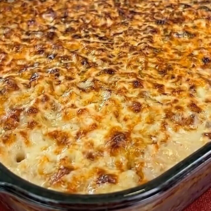A hot spoonful of chicken and mashed potato casserole being lifted from a baking dish, showing melted cheese stretch.