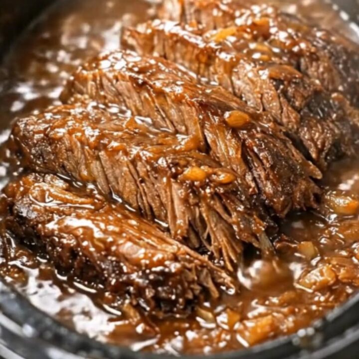 Succulent slow-cooked beef brisket chunks coated in a rich, dark onion gravy in a slow cooker.