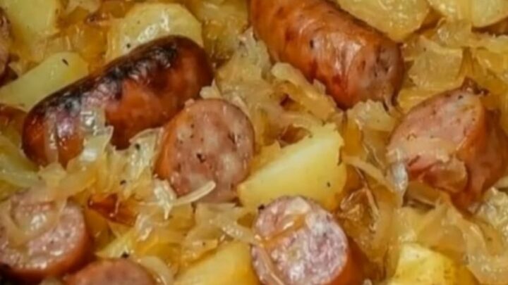 A cast iron skillet filled with browned kielbasa slices, crispy diced potatoes, and steaming sauerkraut.
