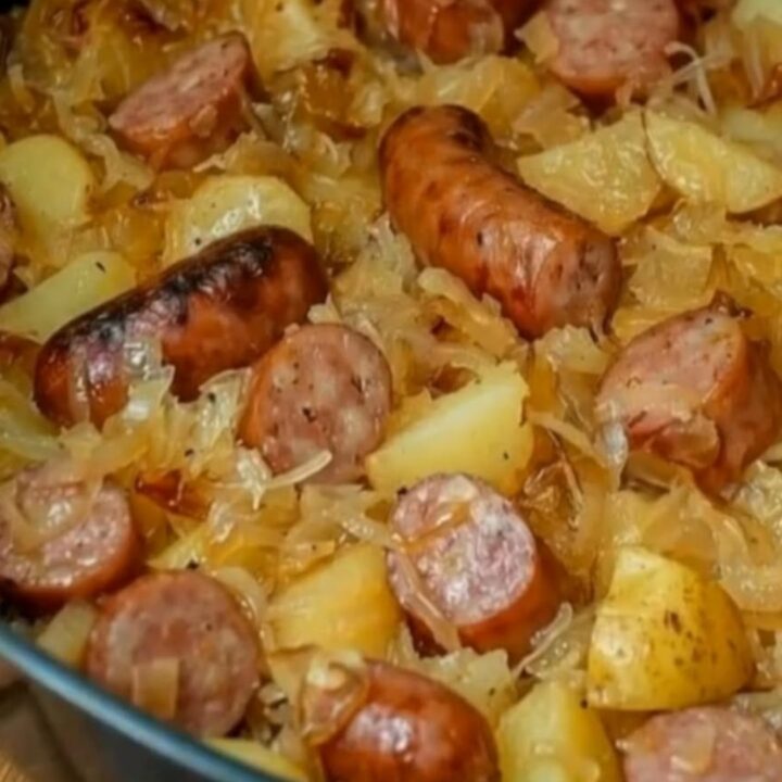 A cast iron skillet filled with browned kielbasa slices, crispy diced potatoes, and steaming sauerkraut.