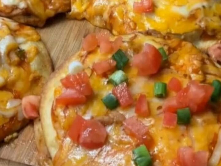 A close-up of a crispy mini Mexican chicken pizza being pulled apart with stretchy melted cheese.