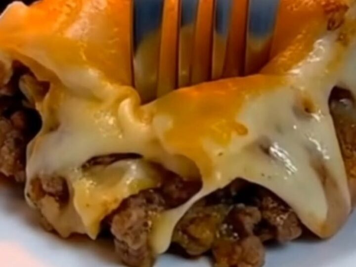 A close-up of a fork sinking into a slice of cheesy Mexican lasagna on a white plate