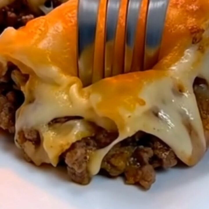 A close-up of a fork sinking into a slice of cheesy Mexican lasagna on a white plate