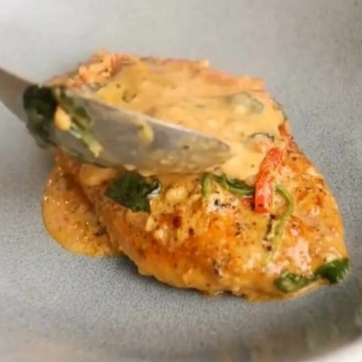 A rustic grey bowl filled with golden-seared chicken breast smothered in a creamy sun-dried tomato and spinach sauce.