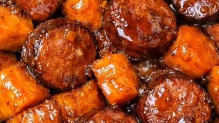 A close-up of a slow cooker filled with glistening, caramelized sweet potato cubes and thick rounds of seared smoked sausage.