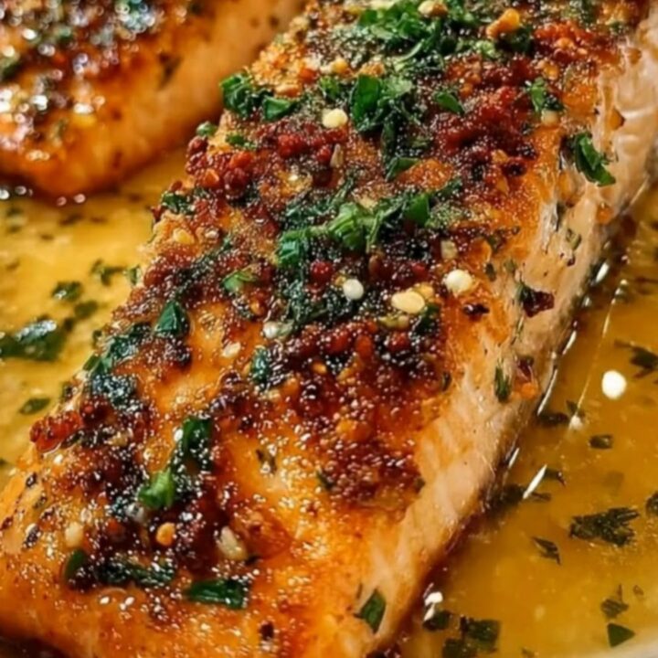 Two perfectly seared salmon fillets topped with a glossy garlic herb butter sauce in a white dish.