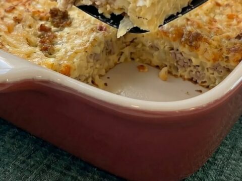A warm, golden-brown slice of breakfast hashbrown and sausage casserole held on a black spatula above the baking dish.