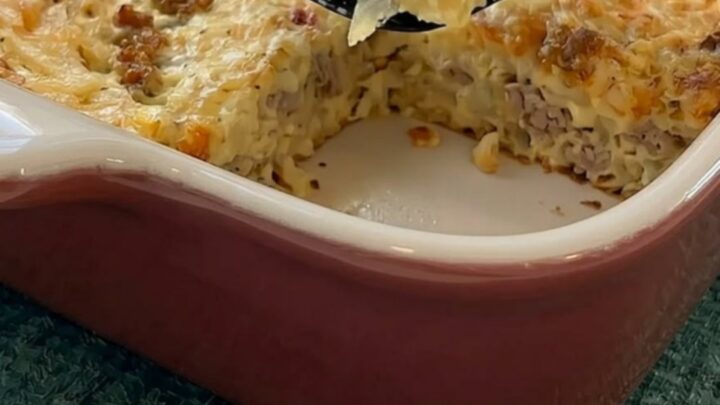 A warm, golden-brown slice of breakfast hashbrown and sausage casserole held on a black spatula above the baking dish.
