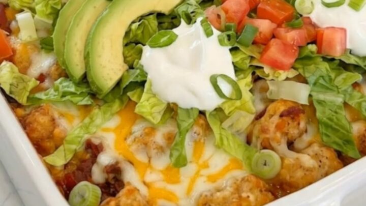 A hearty serving of Cheesy Taco Tater Tot Casserole being lifted from a white ceramic baking dish