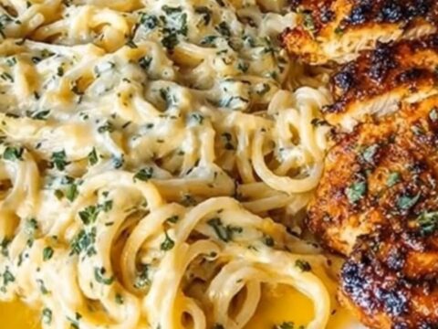 A plate of creamy garlic spaghetti topped with crispy parmesan-crusted chicken slices.