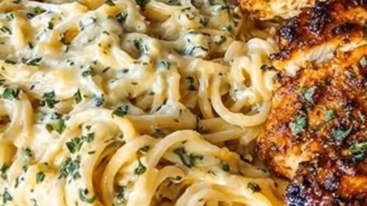 A plate of creamy garlic spaghetti topped with crispy parmesan-crusted chicken slices.
