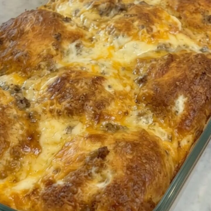 A warm slice of cheesy breakfast biscuit casserole being lifted from a glass baking dish with a spatula.