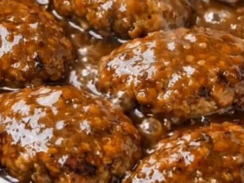 Six glistening Salisbury beef patties gently bubbling in a rich, savory onion and mushroom gravy inside a white slow cooker.