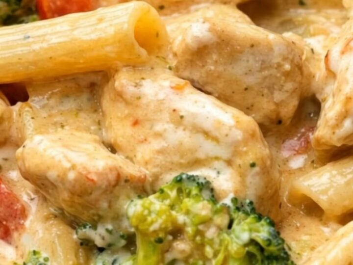 A close-up of creamy chicken penne with bright broccoli and red peppers in a black bowl.