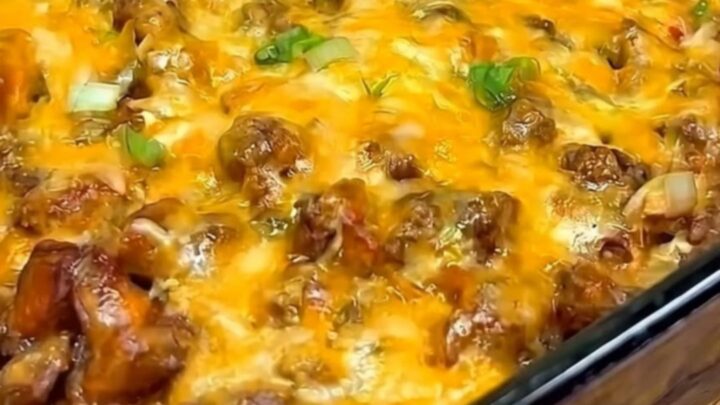 A warm slice of chili cheese dog casserole being scooped from a glass baking dish with a long cheese pull.