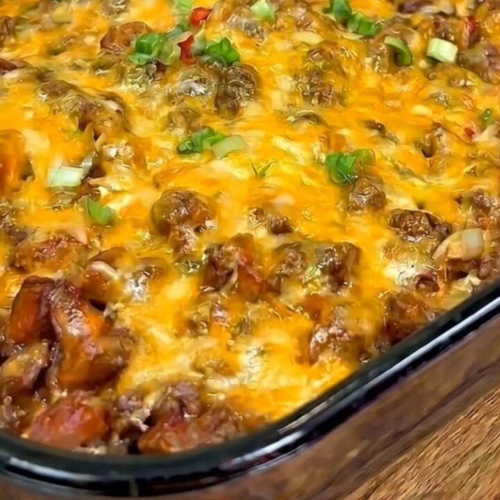 A warm slice of chili cheese dog casserole being scooped from a glass baking dish with a long cheese pull.