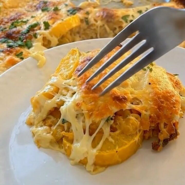 A close-up of a fork lifting a cheesy bite of tender yellow squash casserole with a molten cheese pull.