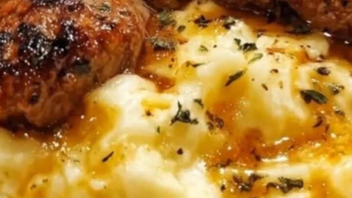 A close-up of seared steak bites resting on a mound of creamy mashed potatoes with melted garlic butter.