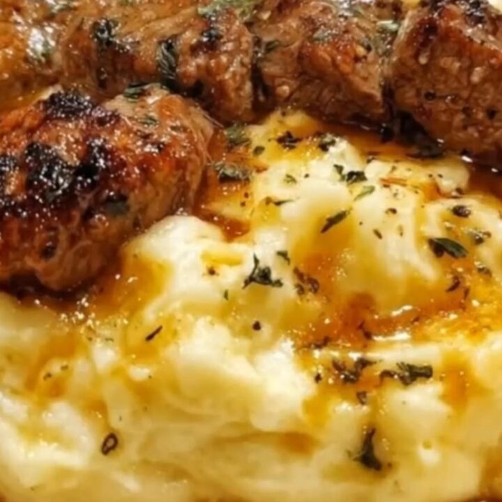A close-up of seared steak bites resting on a mound of creamy mashed potatoes with melted garlic butter.