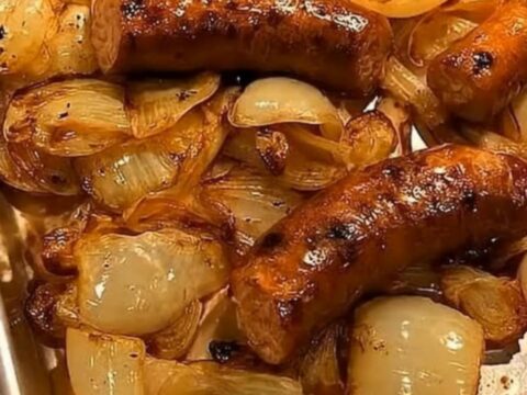 A close-up shot of roasted sausages and caramelized golden onions on a metal baking sheet.