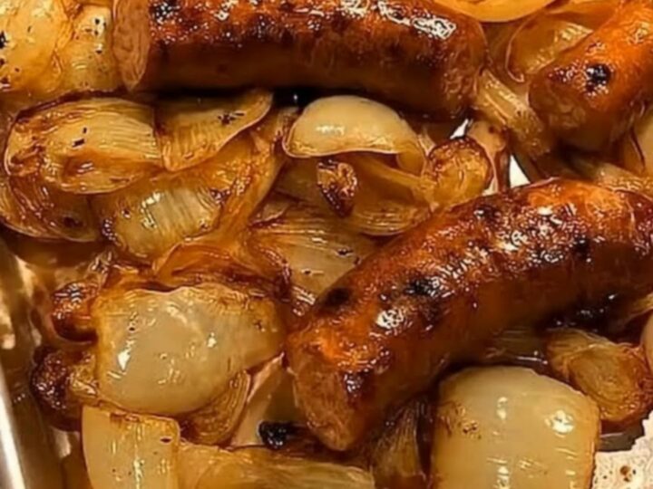A close-up shot of roasted sausages and caramelized golden onions on a metal baking sheet.