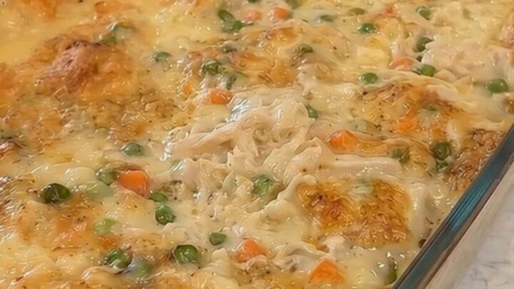 A golden-brown chicken and dumpling casserole steaming in a glass baking dish on a marble counter.