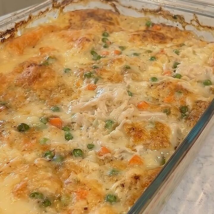A golden-brown chicken and dumpling casserole steaming in a glass baking dish on a marble counter.