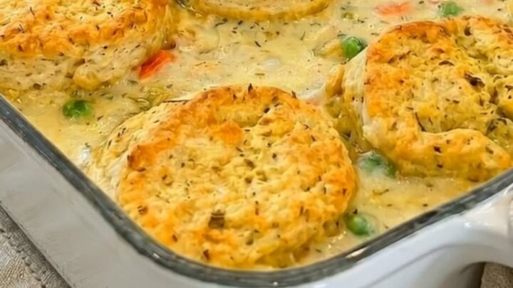 A golden-brown chicken pot pie casserole topped with flaky biscuits in a white baking dish.