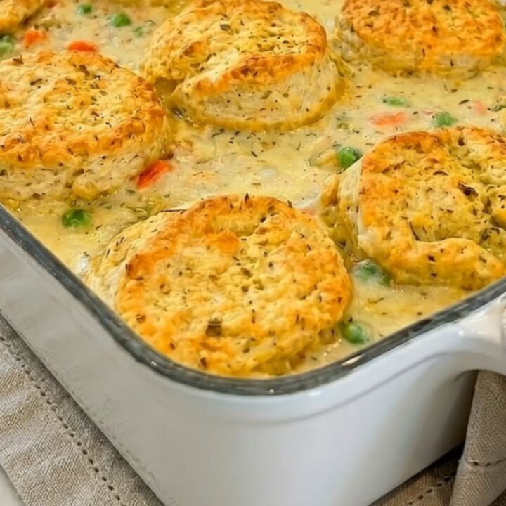 A golden-brown chicken pot pie casserole topped with flaky biscuits in a white baking dish.