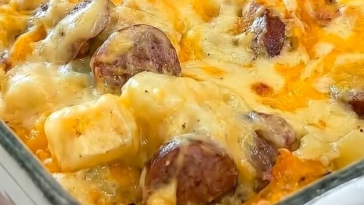 A steaming cheesy potato and sausage casserole in a white dish on a red cloth.