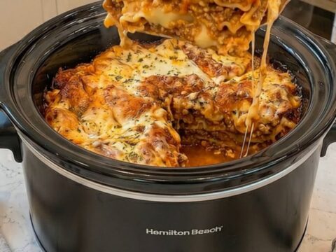 A thick, steaming slice of slow cooker lasagna being lifted with a spatula, showing a long cheese pull.
