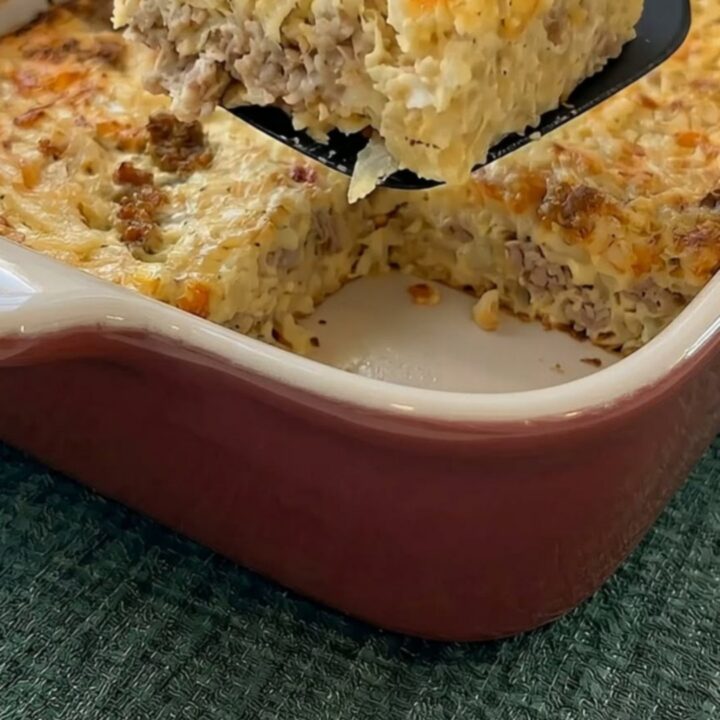 A thick, steaming slice of golden sausage and hash brown breakfast casserole being lifted from a baking dish.