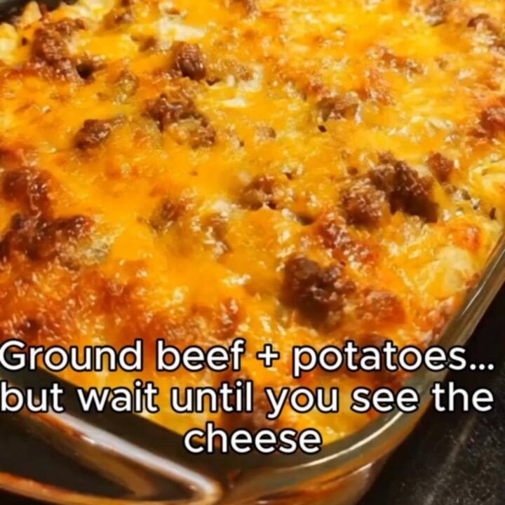 A close-up of a cheesy hamburger and potato casserole with a golden brown melted cheese topping in a glass dish.
