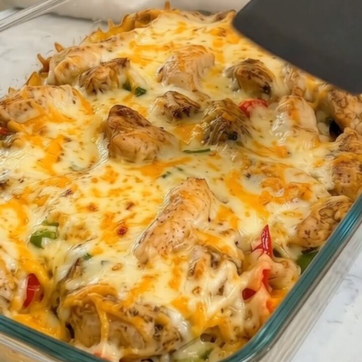 A serving of cheesy chicken fajita rice casserole being lifted from a glass dish with a dramatic cheese pull.