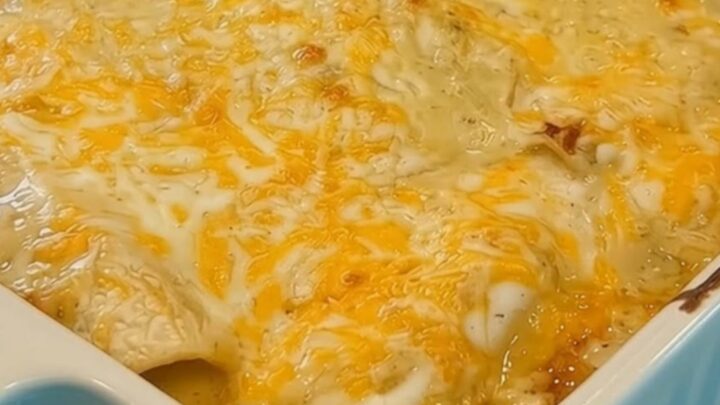 A close-up of a blue baking dish filled with golden, bubbling creamy white chicken enchiladas.