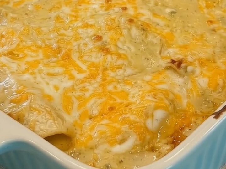 A close-up of a blue baking dish filled with golden, bubbling creamy white chicken enchiladas.